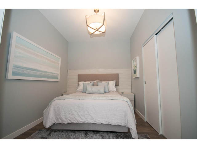 Furnished 1-bedroom with light gray walls, white bedding, and a modern light fixture. - 405 - 105 West 2nd St, North Vancouver