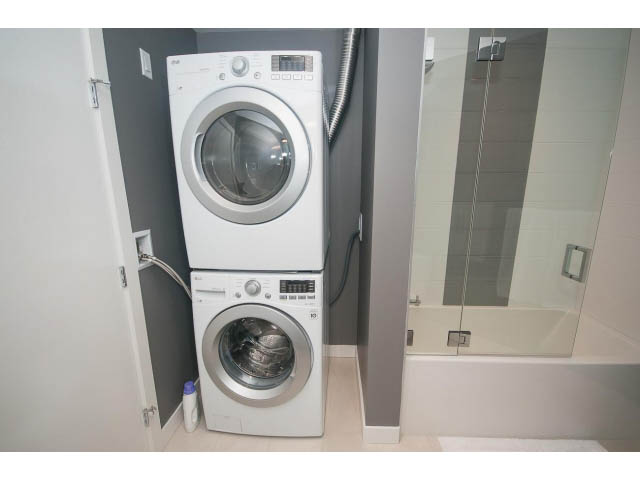 Bright laundry room with white appliances and tiled walls. - 405 - 105 West 2nd St, North Vancouver