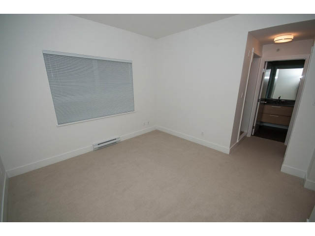 Bright living room with beige carpet and white walls, leading to a kitchen area with dark cabinetry. - 9 - 3508 Mount Seymour Pkwy, North Vancouver