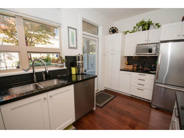 Bright kitchen with white cabinets, black countertops, hardwood floors, and a city view. - 4539 Prince Albert Street, Vancouver East Side