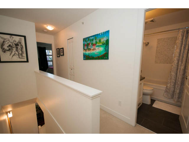 Bright hallway leading to a cozy bathroom with a shower and a bathtub, featuring a colorful painting on the wall.