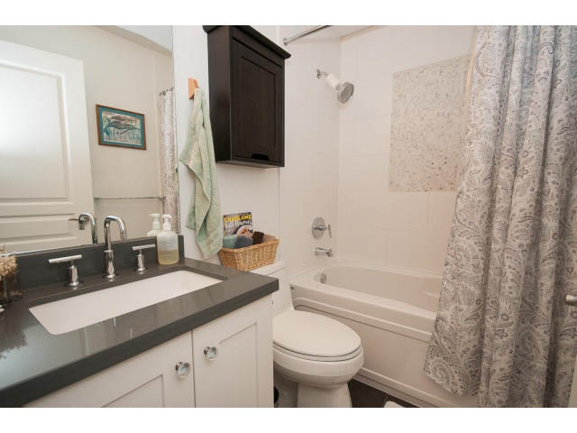 Bright bathroom with dark countertop and white cabinetry, featuring a bathtub and shower. - 4539 Prince Albert Street, Vancouver East Side