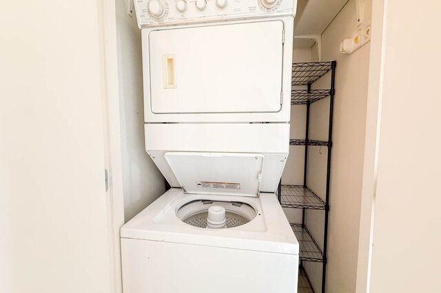 Laundry room with stacked white washer-dryer unit and black wire shelving. - 1605 - 151 West 2nd Street, North Vancouver