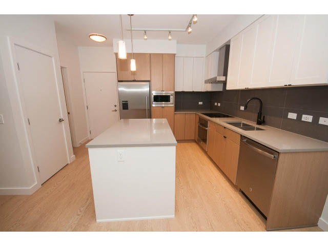 Bright kitchen with white cabinetry, stainless steel appliances, and hardwood floors. - 410 - 3205 Mountain Hwy, North Vancouver