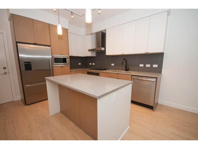 Bright kitchen with white cabinets, stainless steel appliances, and hardwood floors. - 410 - 3205 Mountain Hwy, North Vancouver