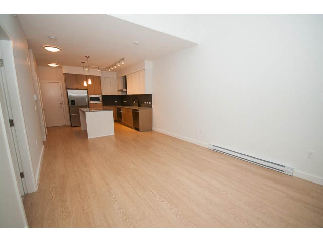 Bright kitchen with white cabinets and hardwood floors, open to a spacious living area. - 410 - 3205 Mountain Hwy, North Vancouver