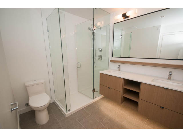 Furnished bathroom with modern glass shower, light wood cabinets, and a large mirror. - 410 - 3205 Mountain Hwy, North Vancouver