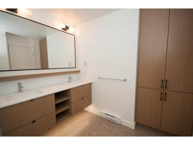Bright bathroom with modern vanity, large mirror, and wooden cabinets. - 410 - 3205 Mountain Hwy, North Vancouver