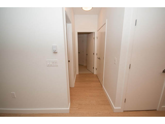 Furnished hallway with light wood flooring and white walls, leading to another room. - 410 - 3205 Mountain Hwy, North Vancouver