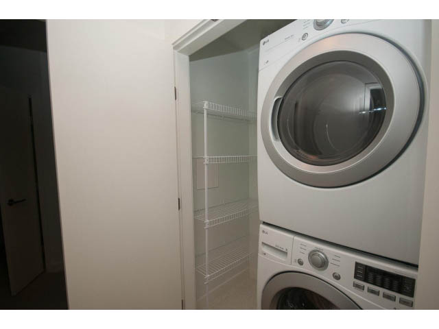 Laundry room with stacked washer and dryer, clear glass door. - 410 - 3205 Mountain Hwy, North Vancouver