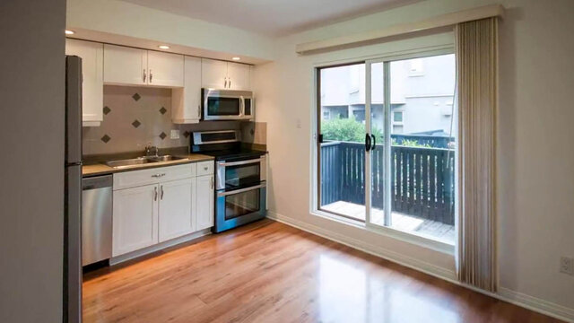 Kitchen with white cabinets, stainless steel appliances, hardwood floors, and a sliding glass door to a balcony.