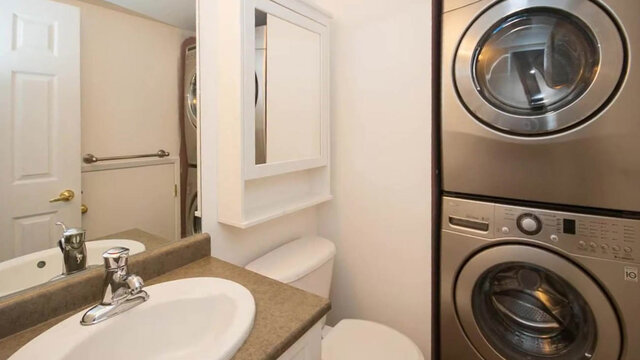 Compact bathroom with granite countertop, white vanity sink, and stacked stainless washer-dryer. - 13-870 West 7th Avenue, Vancouver West Side