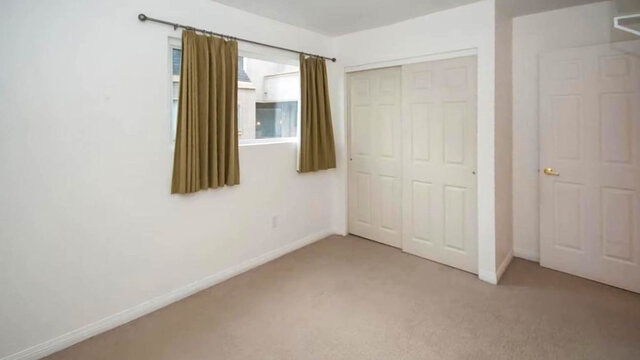 Empty bedroom with beige carpet, white sliding closet doors, and a window dressed in olive curtains. - 13-870 West 7th Avenue, Vancouver West Side