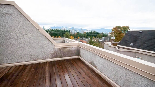 Private rooftop deck with dark wood plank flooring and a distant city-and-mountain view. - 13-870 West 7th Avenue, Vancouver West Side