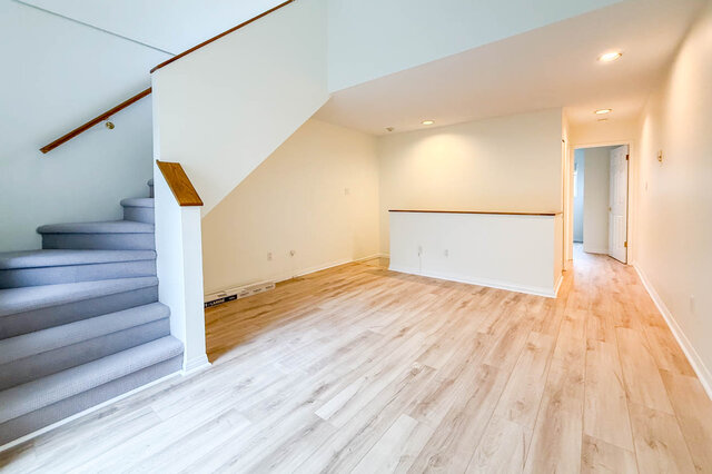 Open middle-level living room with hardwood floors, pot lights, a half wall with wood cap and carpeted stairs rising to the l
