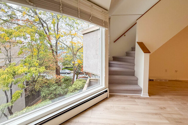 Large corner picture window in the living room framing golden autumn treetops and the leafy street below, beside the stairs u