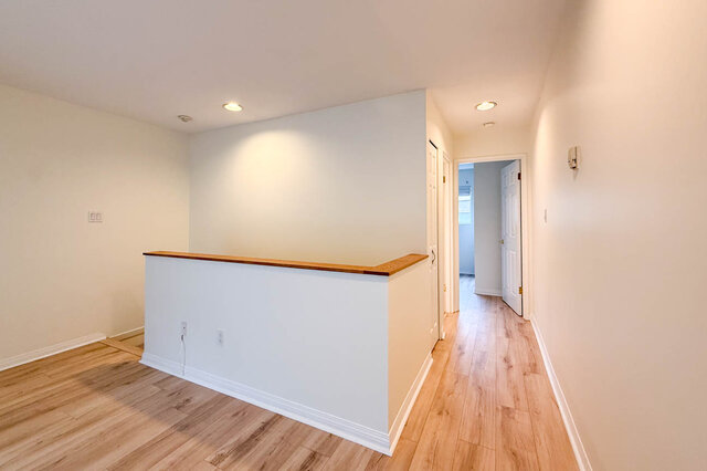 Middle-level hallway with a half wall topped in wood, hardwood floors and doors to the bedroom and bathroom.