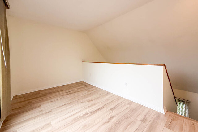 Top-floor loft den under a sloped ceiling, hardwood floors and a half wall with wood cap overlooking the stairwell.
