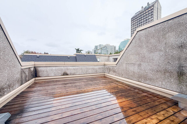 Large private rooftop deck with cedar-toned wood decking, low stucco walls and city towers rising over the rooftops.