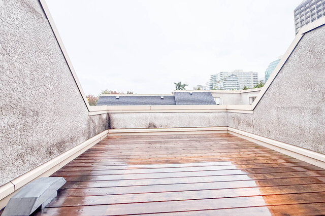 Private rooftop deck seen end to end, wood decking framed by stucco walls, open sky and city towers in the distance.