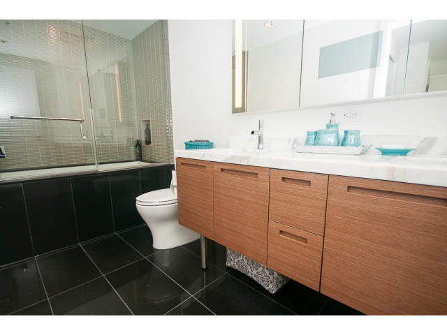 Modern bathroom with wooden cabinets, black tile flooring, and a large mirror. - 4609 - 777 Richards St, Vancouver Downtown