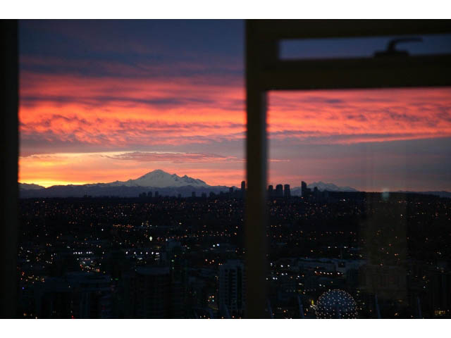 Bright living room with stunning city view at sunset, featuring a vibrant sky and distant mountains. - 4609 - 777 Richards St, Vancouver Downtown