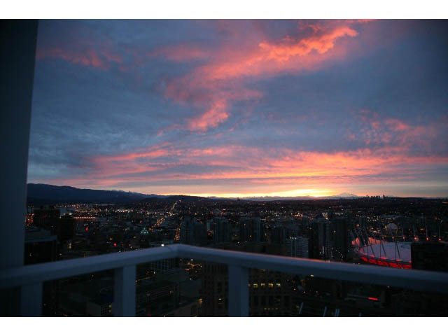 Bright balcony with stunning city view at sunset, featuring vibrant sky and distant mountains. - 4609 - 777 Richards St, Vancouver Downtown