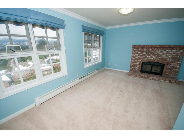 Bright living room with large windows and a brick fireplace, offering a city view. - 4220 Starlight Way, North Vancouver