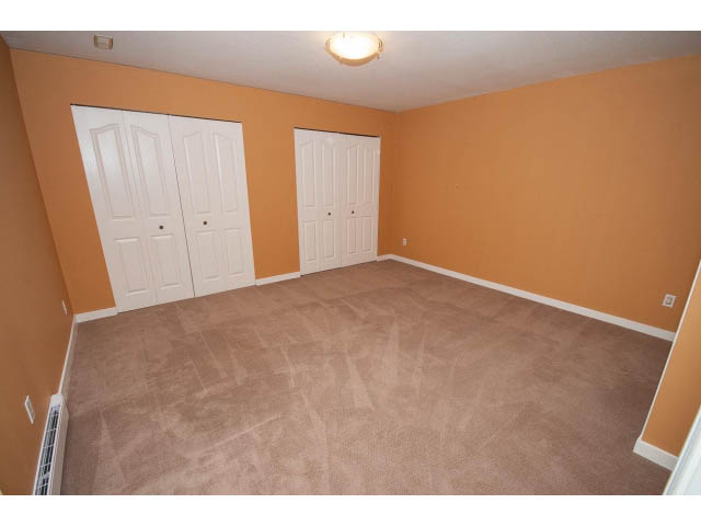 Spacious bedroom with orange walls, carpeted floor, and white closet doors. - 4220 Starlight Way, North Vancouver