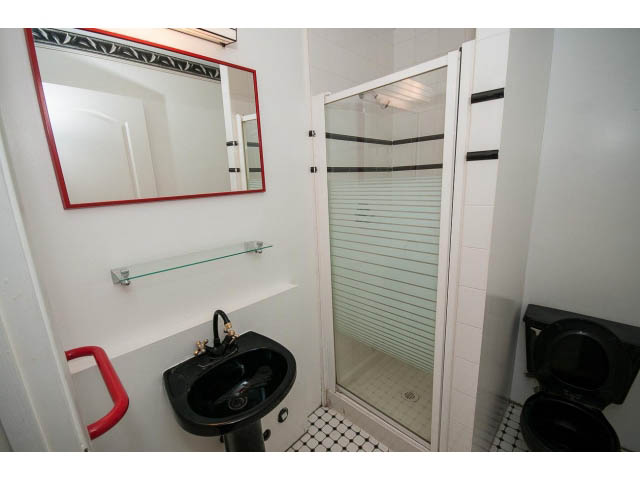 Small bathroom with black and white tile, glass shower door, and red-framed mirror. - 4220 Starlight Way, North Vancouver