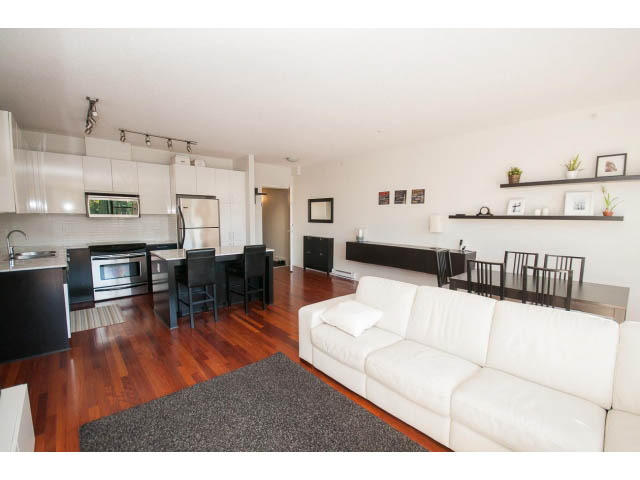 Spacious penthouse living room with white leather couch, hardwood floors, and modern kitchen appliances. - 401 - 2828 Yew St, Vancouver West Side