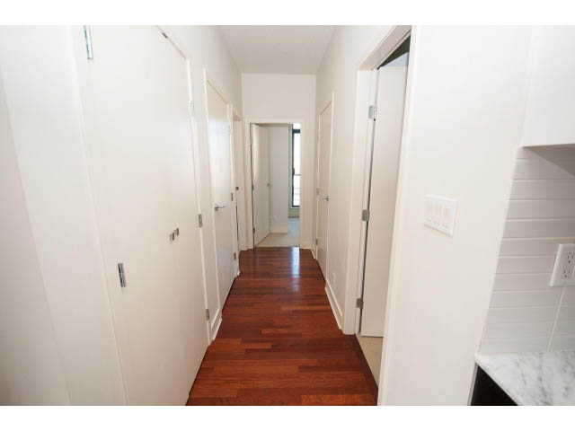 Bright hallway with hardwood floors and white walls leading to a room with a marble countertop. - 401 - 2828 Yew St, Vancouver West Side