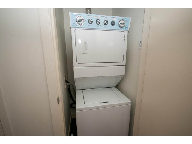 Bright laundry room with stacked washer and dryer, white cabinets. - 401 - 2828 Yew St, Vancouver West Side