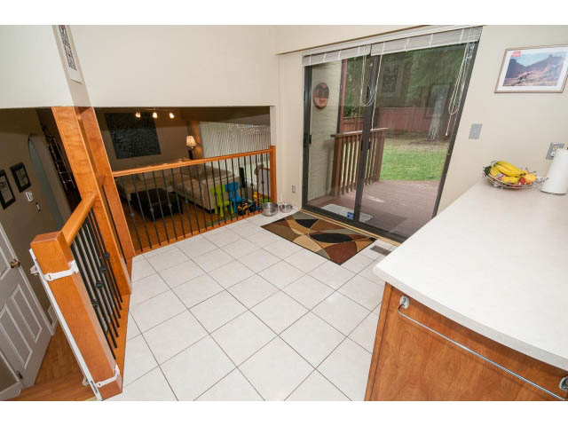 Bright kitchen with white countertops and hardwood floors, leading to a patio with sliding glass doors. - 2346 Riverbank Place, North Vancouver