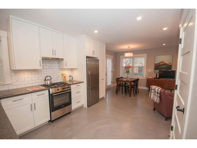 Bright kitchen with white cabinets, stainless steel appliances, and a cozy living area with a red couch and wooden coffee...