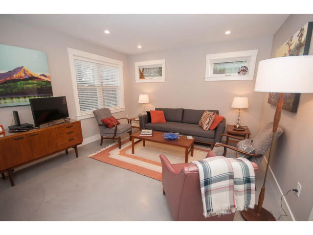 Furnished living room with cozy furniture, plaid throw, and mountain painting. - 2 - 217 East 19th, North Vancouver