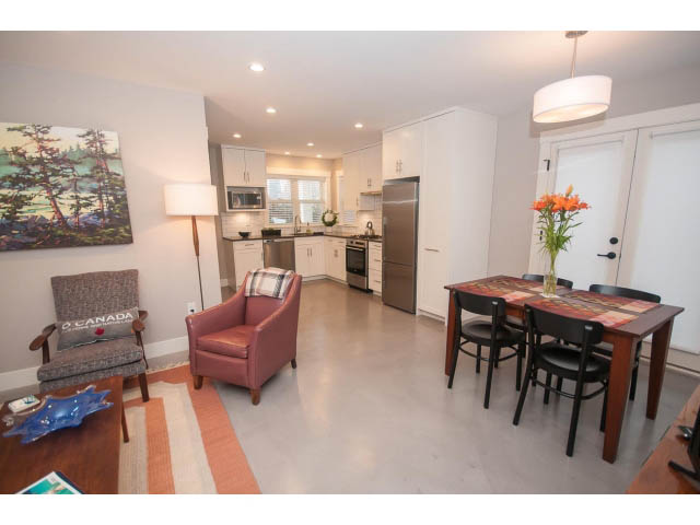 Bright kitchen with stainless steel appliances and hardwood floors, leading to a cozy dining area with a vase of flowers.