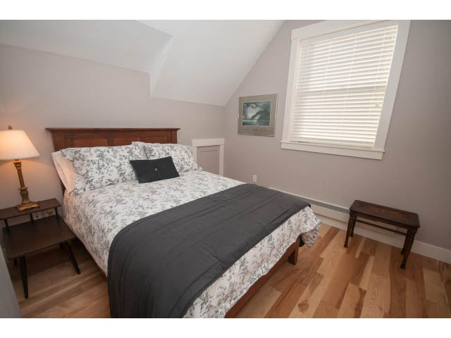 Furnished bedroom with hardwood floors and a cozy bed setup. - 2 - 217 East 19th, North Vancouver