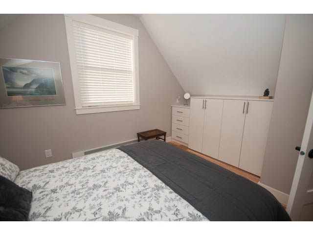 Bright bedroom with white cabinets, floral bedspread, and hardwood floors. - 2 - 217 East 19th, North Vancouver