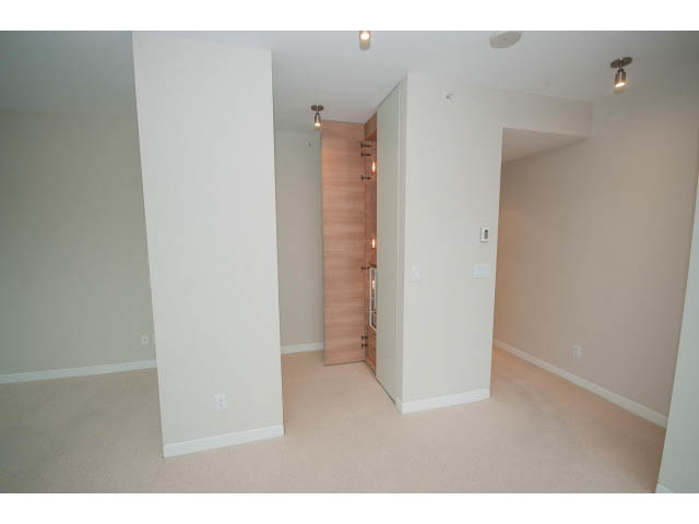 Bright living room with beige carpet and white walls, leading to a hallway with wooden doors. - 1902 - 838 W Hastings, Vancouver Downtown