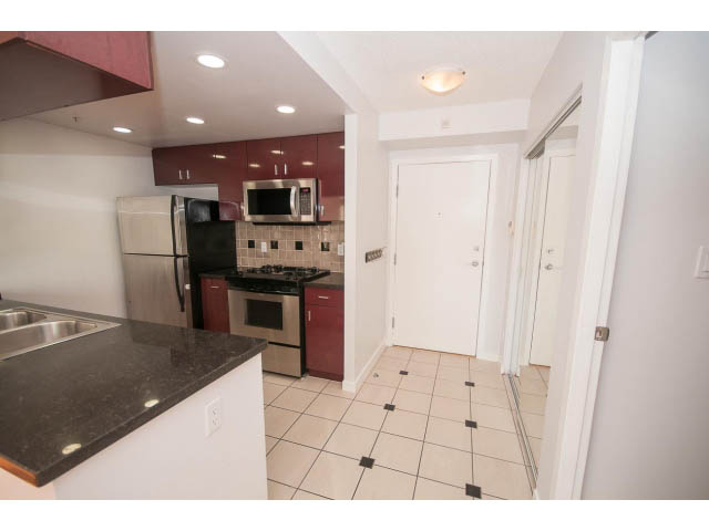 Bright kitchen with dark granite countertops and red cabinets, open to a dining area. - 2005 - 1067 Marinaside Crescen, Vancouver Downtown