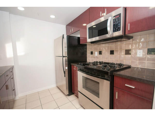 Bright kitchen with stainless steel appliances and red cabinets, featuring a gas stove and microwave.