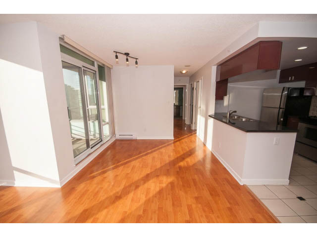 Bright kitchen with dark countertops and hardwood floors, leading to a spacious living area with a city view.