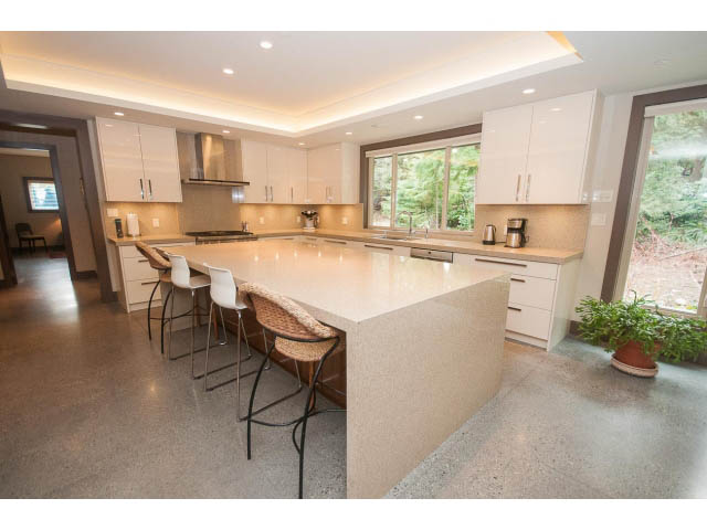 Bright kitchen with light-colored countertops and hardwood floors, featuring a large window with a view of greenery.