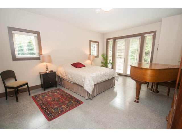 Spacious bedroom with two beds, wooden furniture, and a red rug. - 5070 Marine Drive, West Vancouver