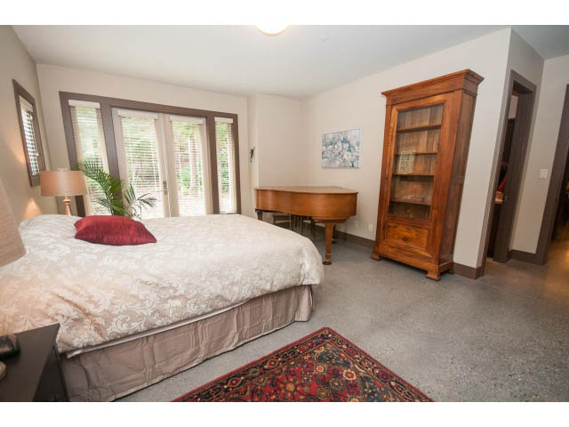 Spacious bedroom with large windows, wooden furniture, and patterned rug. - 5070 Marine Drive, West Vancouver