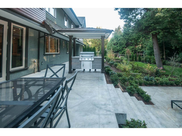 Spacious patio with modern grill and outdoor seating, surrounded by lush greenery. - 5070 Marine Drive, West Vancouver