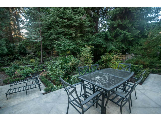 Furnished patio with outdoor tables and chairs, surrounded by lush greenery. - 5070 Marine Drive, West Vancouver