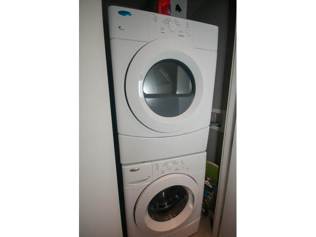 Bright laundry room with stacked washer and dryer, white cabinets. - 1702 - 135 East 17th Street, North Vancouver