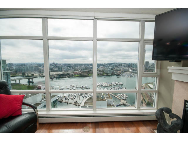 Bright living room with large windows offering a stunning city view, hardwood floors, and a modern TV setup.